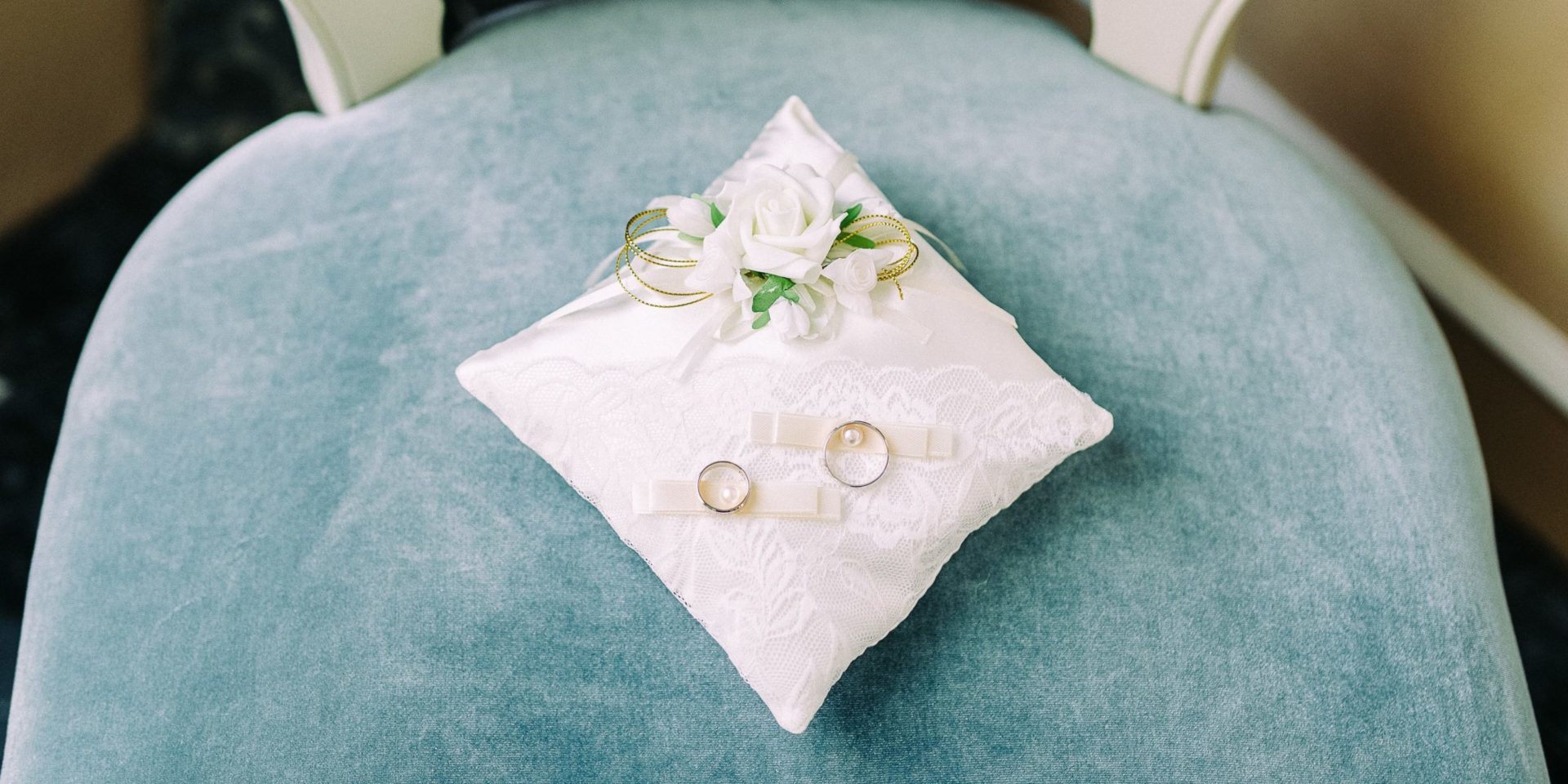 Two wedding rings sit on a decorative, white lace ring pillow.