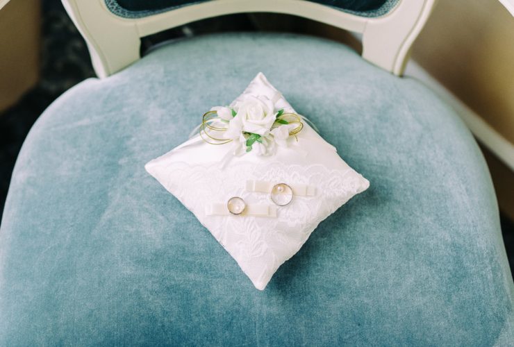 Two wedding rings sit on a decorative, white lace ring pillow.